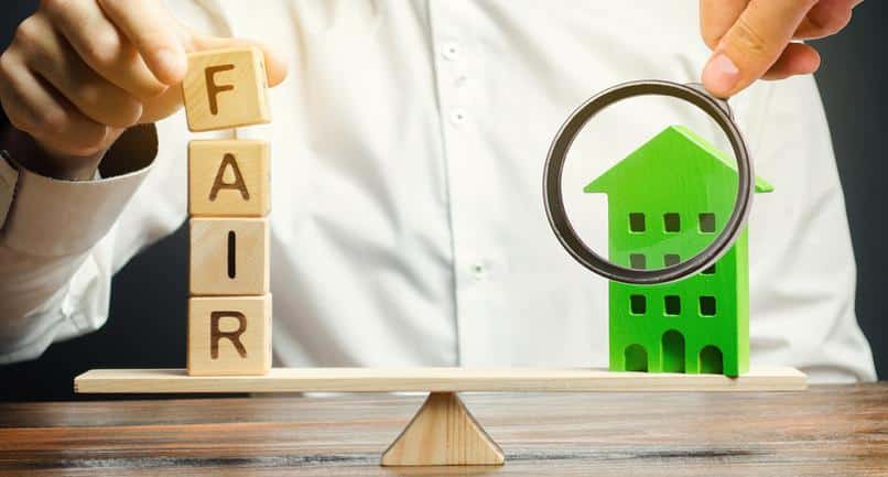 Wooden blocks with the word Fair and a wooden house. Fair value of real estate and housing. Property valuation. Home appraisal. Housing evaluator. Legal transparent deal. Apartment purchase / sale. Fair Housing Balance Magnifying Glass