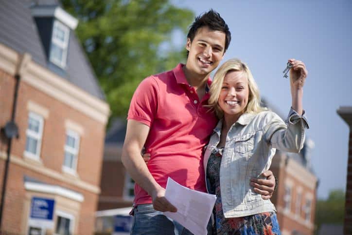 Young couple as first time home buyers holding up a key to their new home