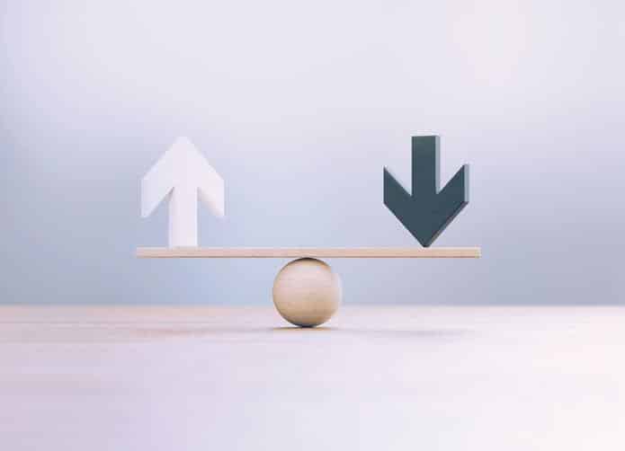 White And Black Wooden Arrow Symbols Sitting Over Wooden Seesaw Scale Before Defocused Background