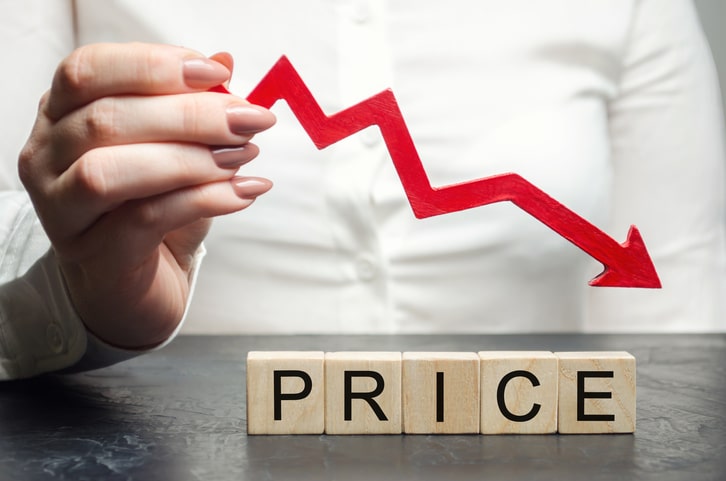 A woman holds a red arrow down over wooden blocks and the word Price. Concept of falling market value. Promotions and sale. Reduced prices for housing and food. Dumping. Low prices