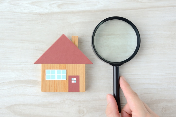 House object and human’s hands with magnifying glass on natural wooden table