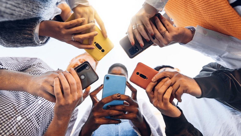 Teens in circle holding smart mobile phones – Multicultural young people using cellphones outside – Teenagers addicted to new technology concept