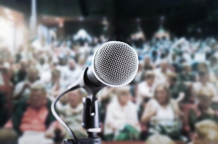 Vocal microphone awaiting public speaker, singer or actor in a crowded theater, with blurred audience waiting for the show