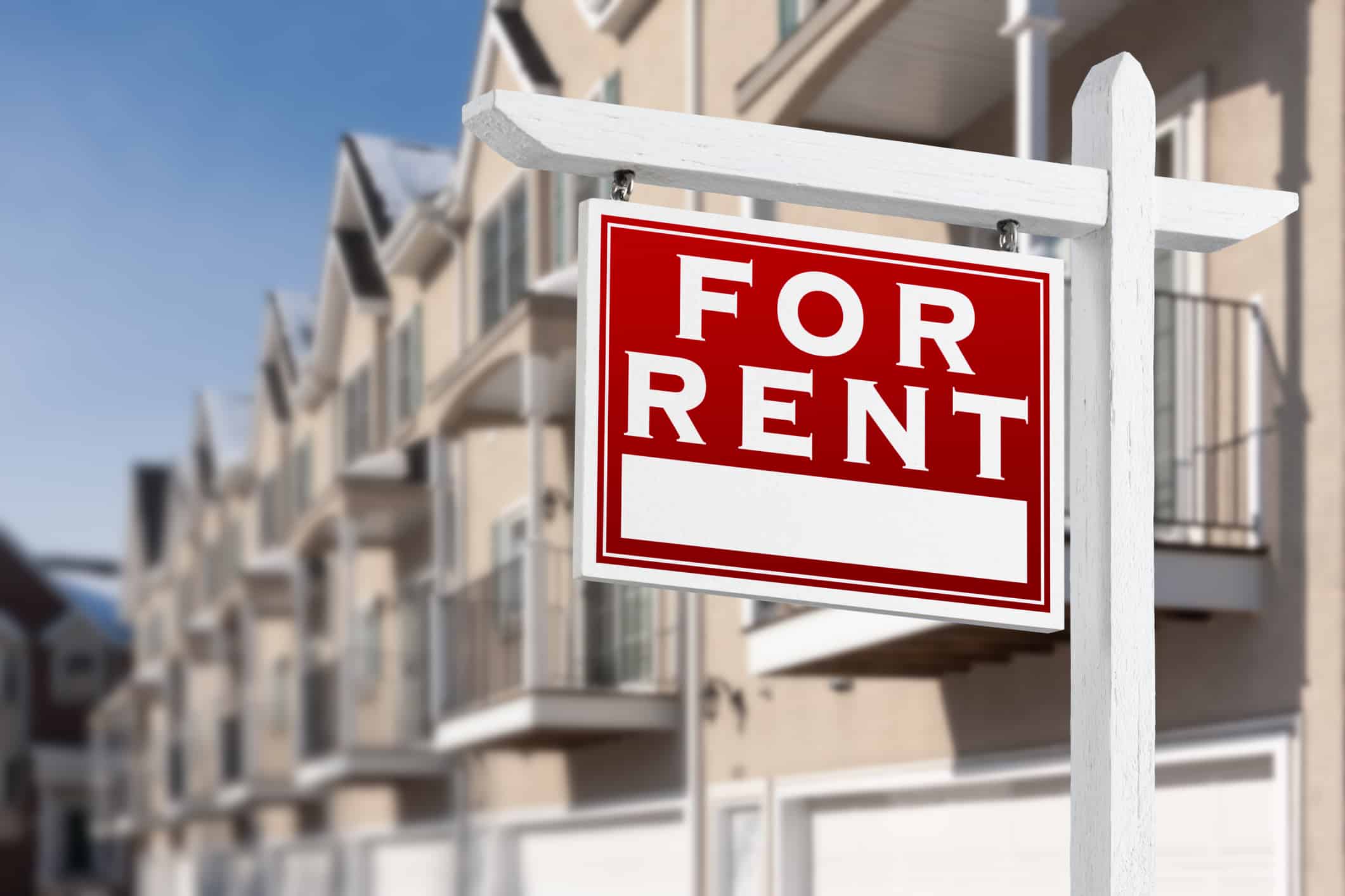 For Rent Real Estate Sign In Front of a Row of Apartment Condominiums Balconies and Garage Doors. home for rent